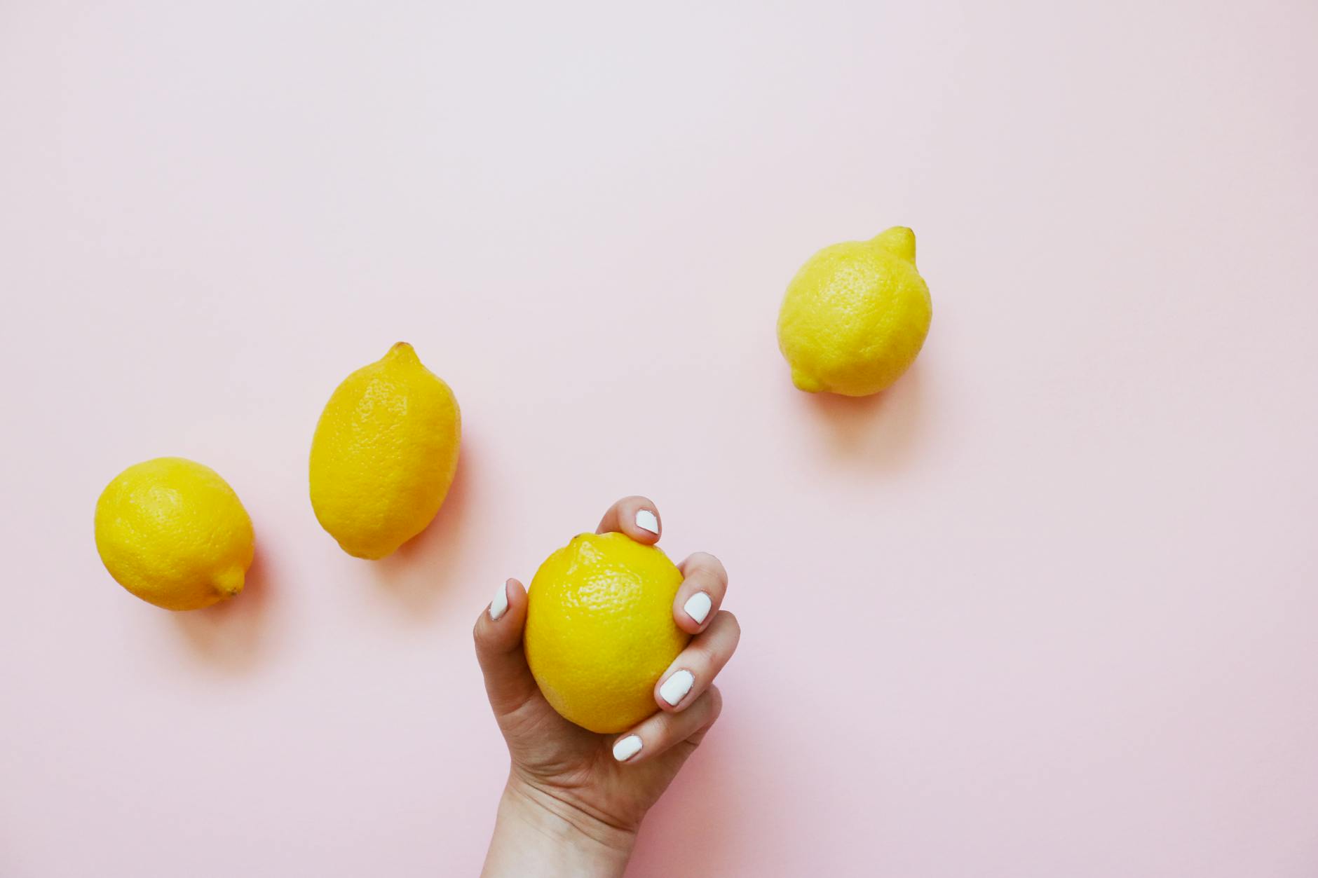 Hand holding a fresh lemon on soft pink background with additional lemons