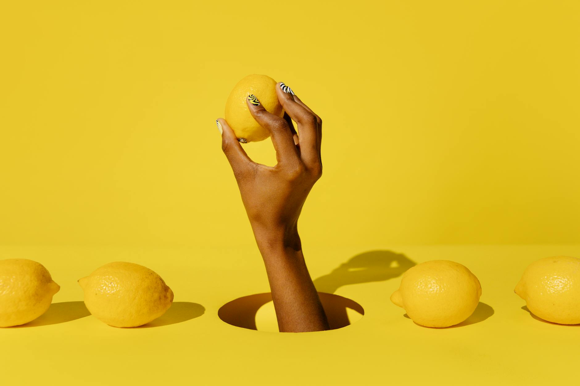 Close-up of a hand holding a lemon against a vivid yellow background