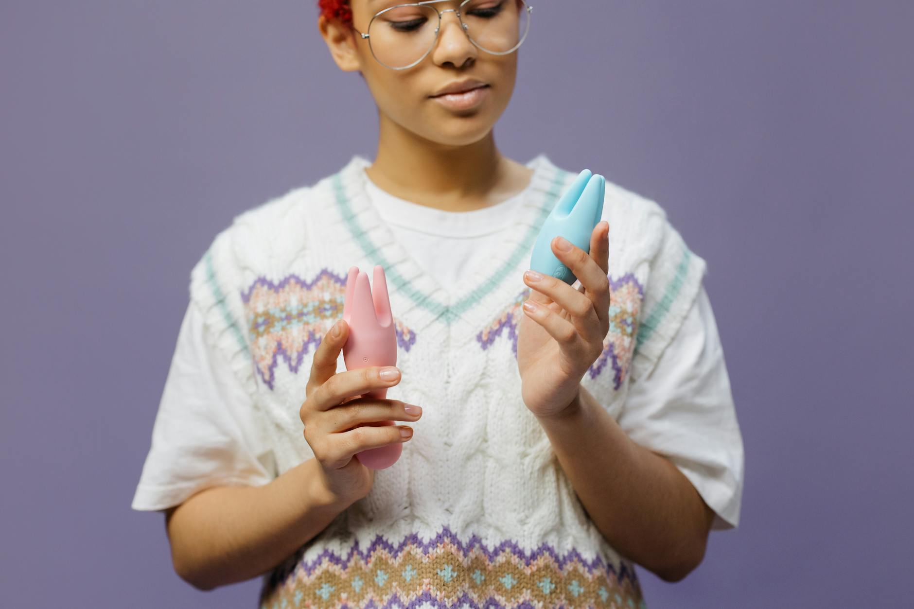 Woman holding blue and pink silicone vibrators thoughtfully