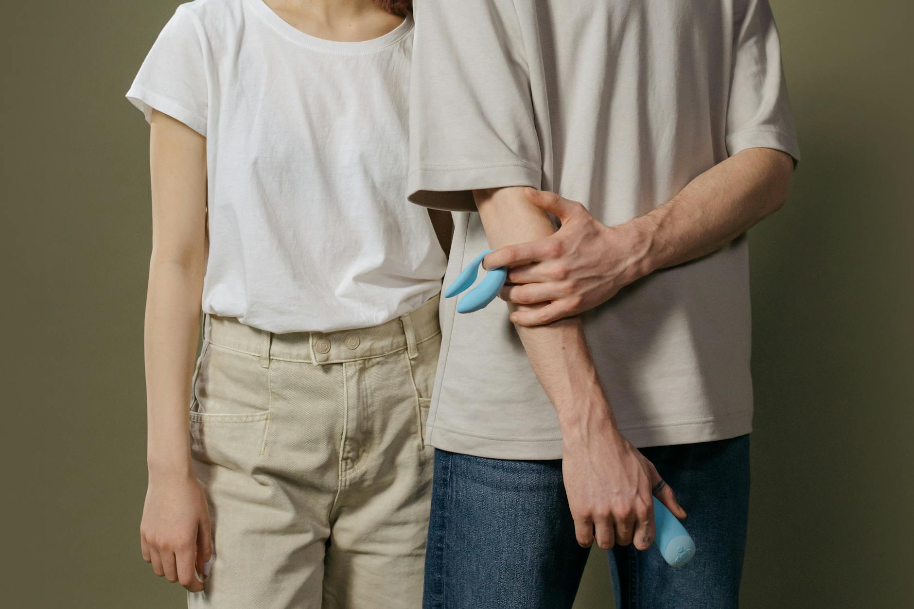 A young couple standing together indoors, holding a blue vibrator, symbolizing modern intimacy and communication about sexual wellness.